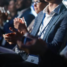 istockphoto-1482843873-612x612 Close Up on Hands of a Crowd of People Clapping in Dark Conference Hall During a Motivational Keynote Presentation. Business Technology Summit Auditorium Room Full of Delegates.